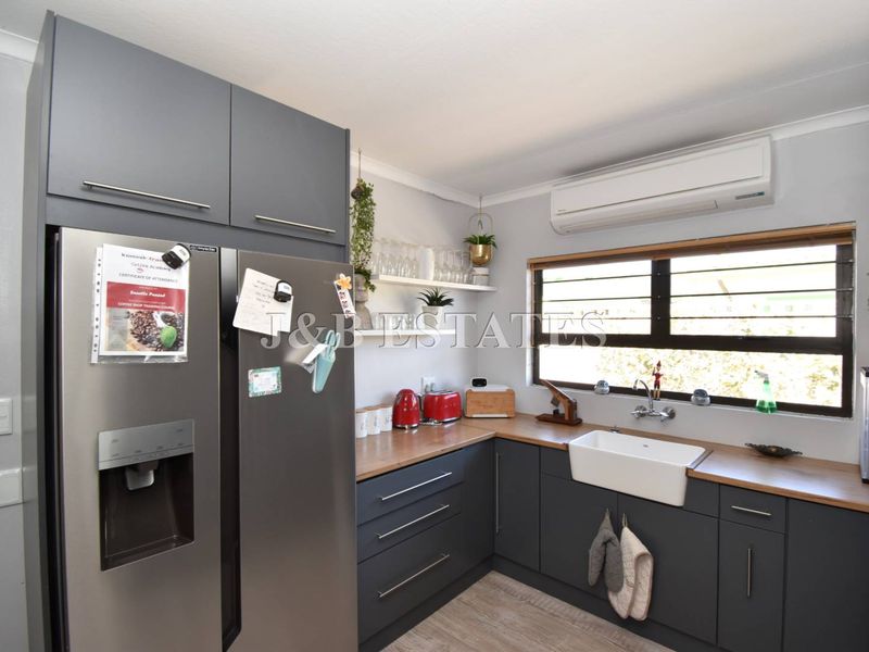 Modern kitchen featuring dark grey cabinetry, wooden countertops, a classic farmhouse sink, and a wall-mounted air conditioning unit.