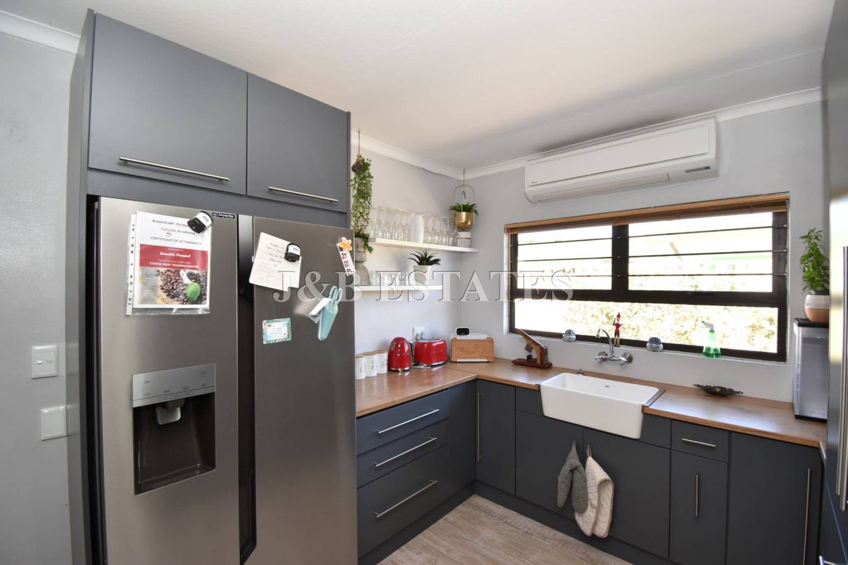 Modern kitchen featuring dark grey cabinetry, wooden countertops, a classic farmhouse sink, and a wall-mounted air conditioning unit.