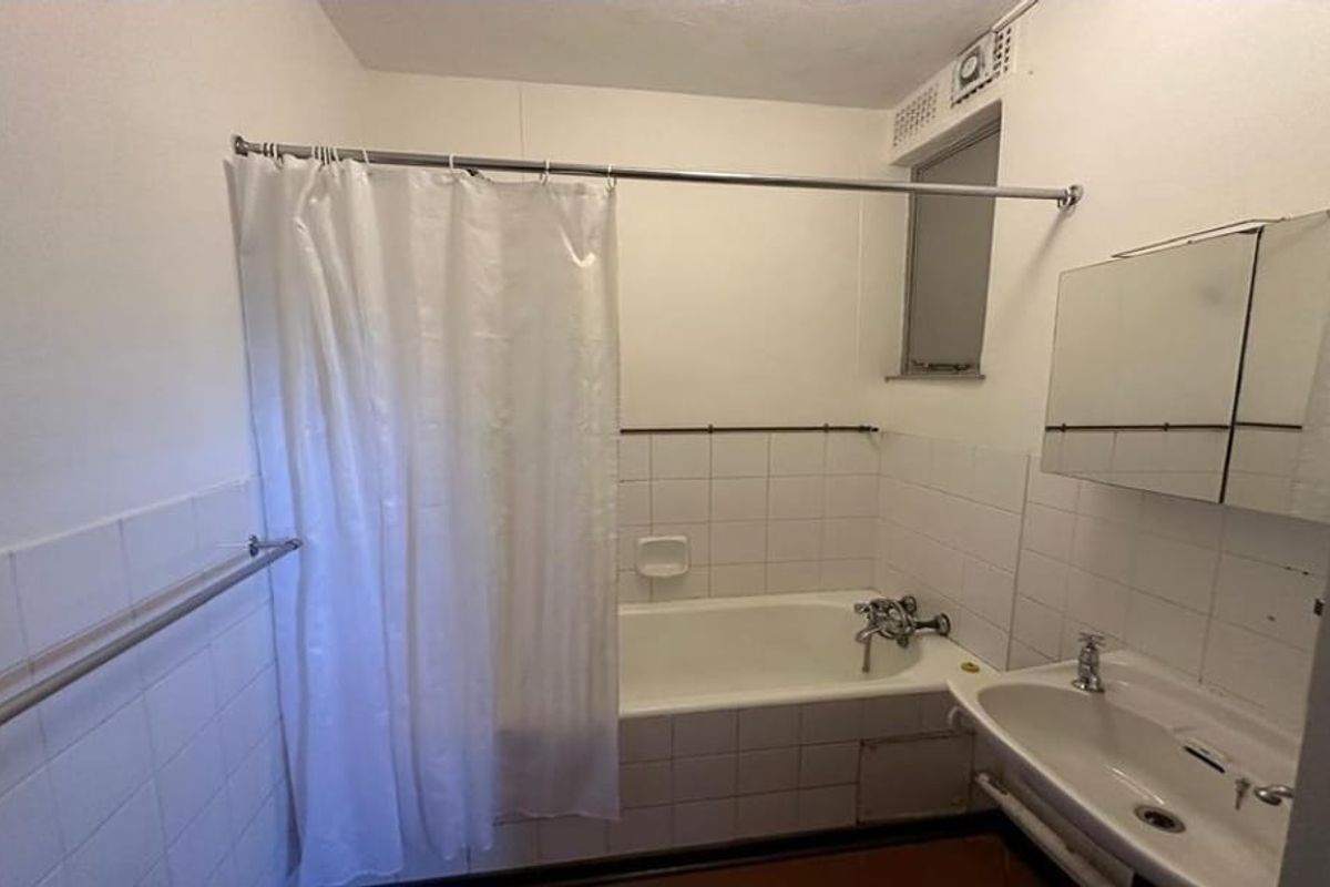 A functional bathroom featuring a bathtub with shower attachment, wall-mounted basin, and medicine cabinet, requiring cosmetic updates to modernize the space.