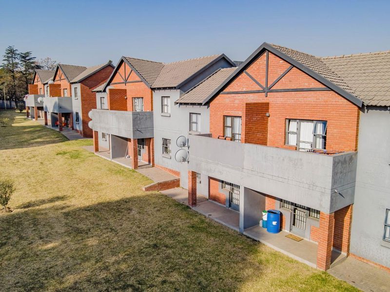 An aerial view of a multi-unit apartment complex featuring brick and rendered facades, tiled roofs, and private balconies overlooking a communal lawn area.