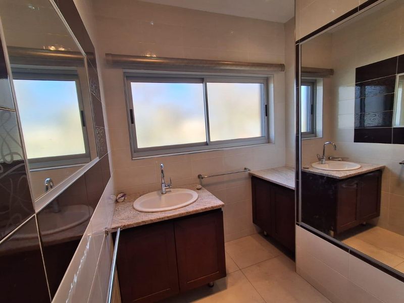 A clean, well-maintained bathroom featuring a double vanity with granite countertops, large wall mirrors, and neutral tiled finishes.