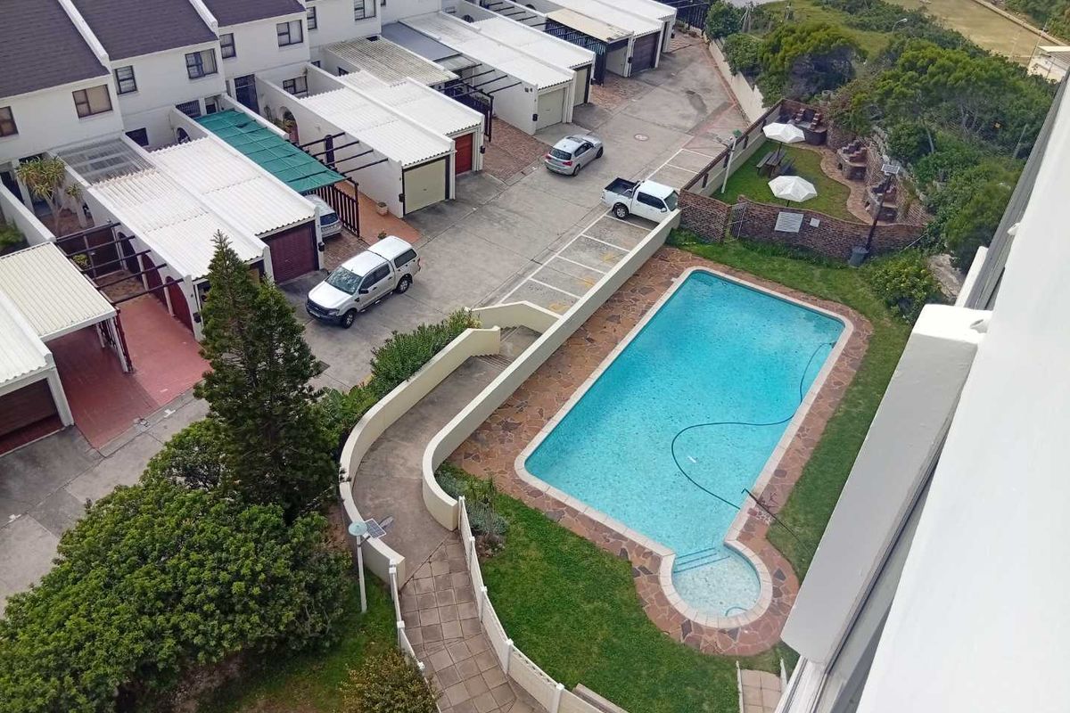 Aerial view of the apartment complex featuring a communal swimming pool, landscaped garden areas, and a paved driveway with garage access.