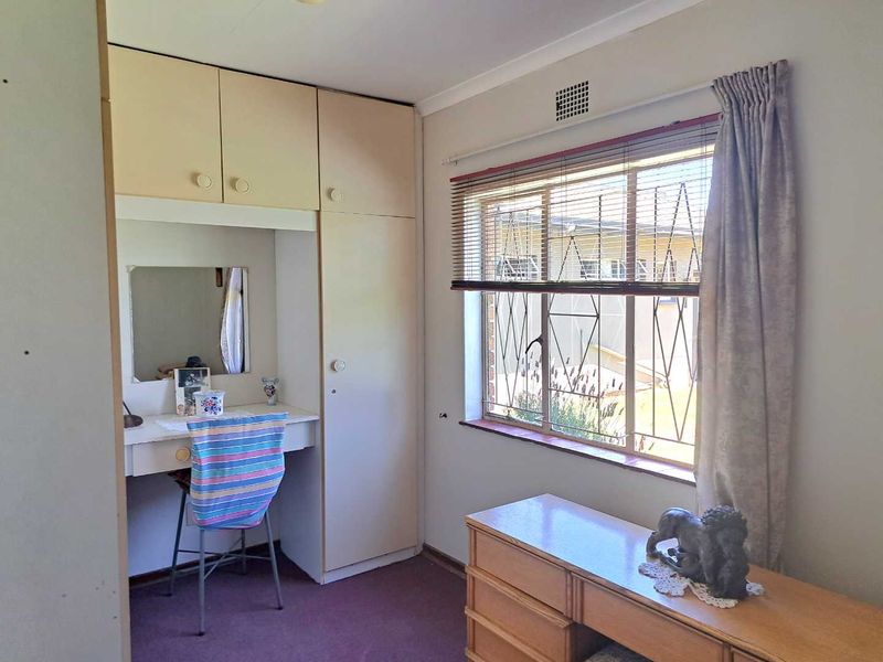 Bedroom featuring built-in cupboards with an integrated vanity unit, security bars on the window, and carpeted flooring.