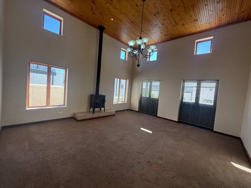 Spacious living room featuring a high vaulted timber ceiling, a freestanding wood-burning fireplace on a tiled hearth, and abundant natural light through large windows.