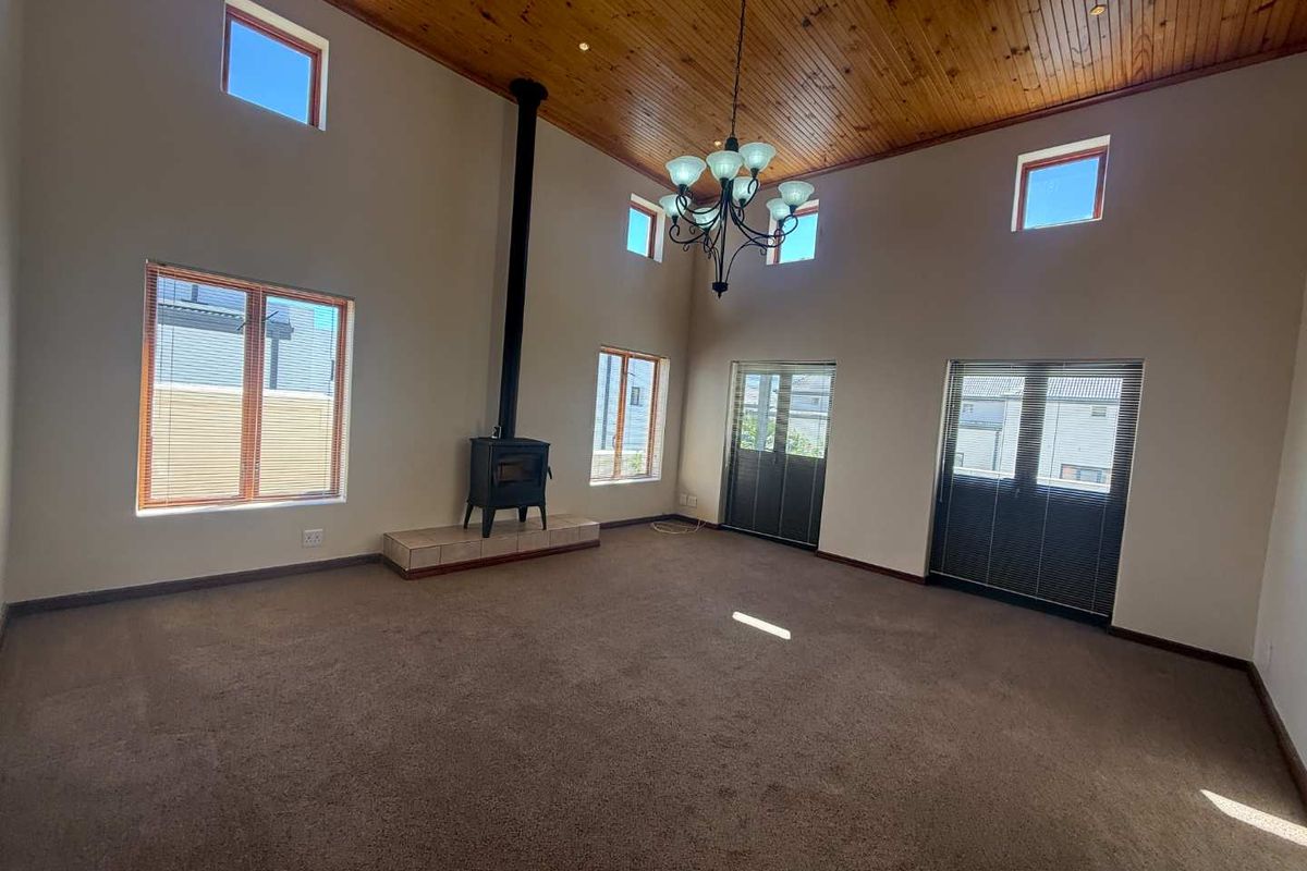 Spacious living room featuring a high vaulted timber ceiling, a freestanding wood-burning fireplace on a tiled hearth, and abundant natural light through large windows.