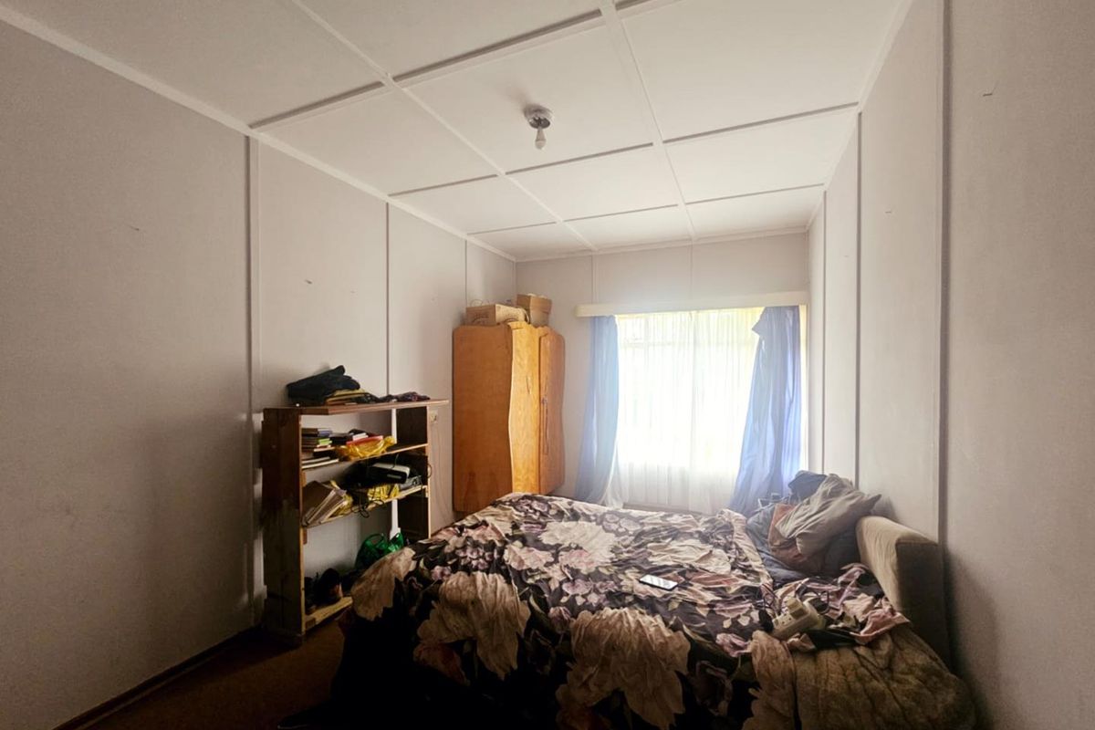 A bedroom featuring panelled walls and a tiled ceiling, offering a functional space with natural light from the window.