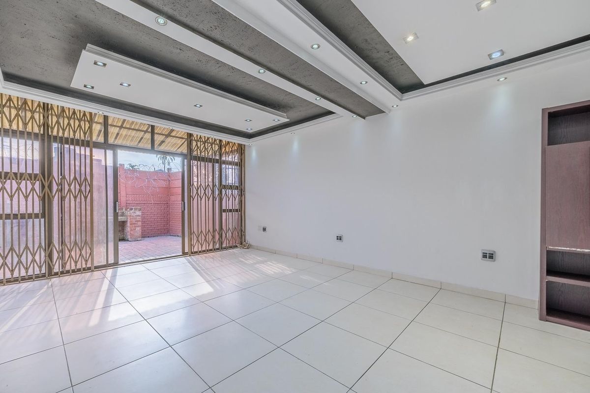 Spacious living area featuring modern recessed ceiling lighting, large format floor tiles, and a sliding glass door leading to an outdoor patio area.