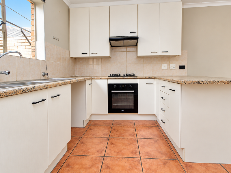 A functional kitchen featuring white cabinetry, granite countertops, a built-in oven with gas hob, and tiled flooring.