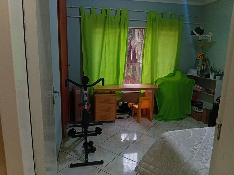 A bedroom featuring tiled flooring and a window with curtain rods, providing a functional space for rest or study.