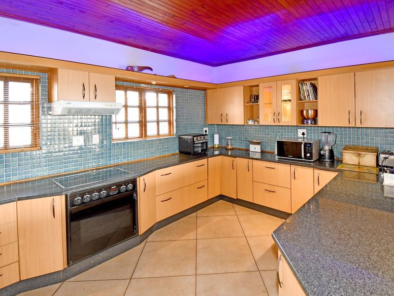 A functional kitchen featuring light wood cabinetry, granite countertops, a tiled backsplash, and a distinctive timber ceiling with integrated accent lighting.