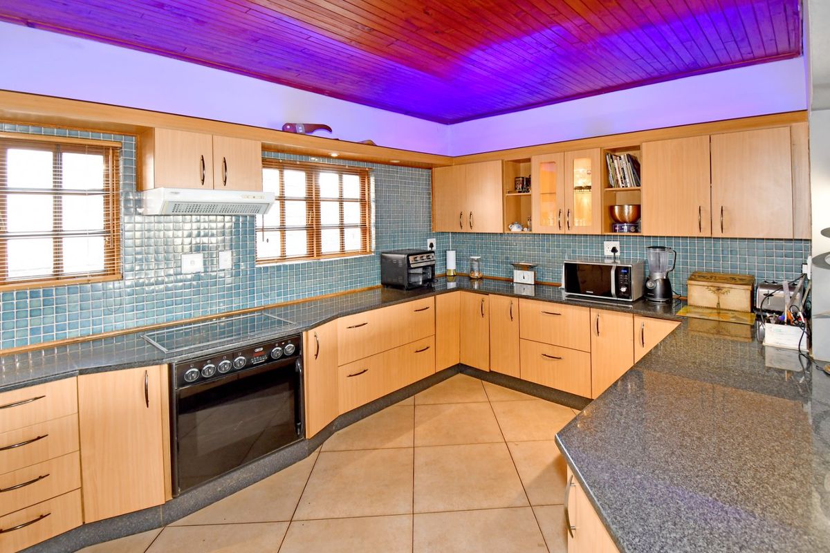 A functional kitchen featuring light wood cabinetry, granite countertops, a tiled backsplash, and a distinctive timber ceiling with integrated accent lighting.