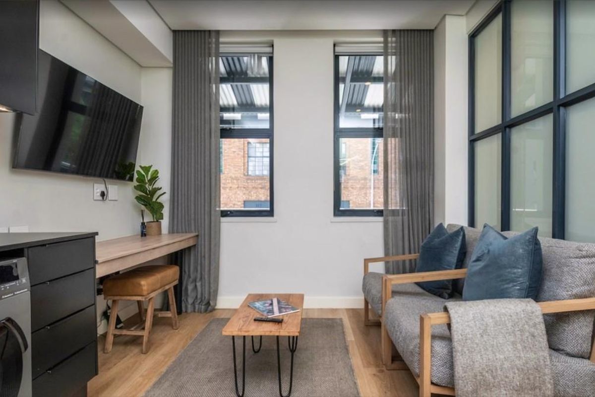 A modern, compact living area featuring timber flooring, built-in desk space, and large windows with integrated curtain tracks.