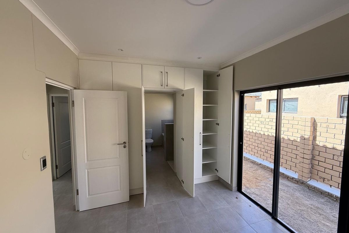 A bright bedroom featuring built-in cupboards, tiled flooring, and sliding glass doors leading to an outdoor area, with an en-suite bathroom access.