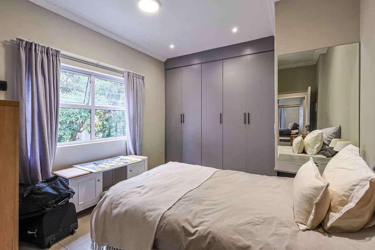 A well-maintained bedroom featuring neutral tones, ample built-in cupboard storage, and large windows that provide natural light.