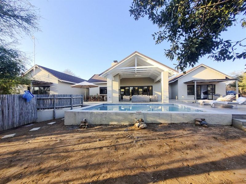 A rear view of the property featuring a swimming pool, timber decking, and a spacious covered patio area with large sliding glass doors.