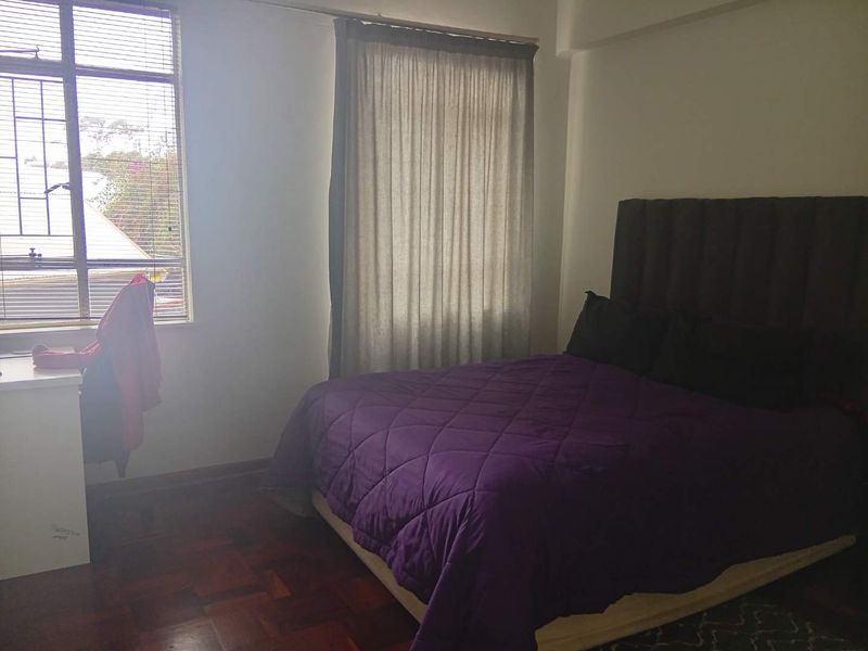 A bedroom featuring parquet flooring and a window with security bars, providing natural light and a functional layout.