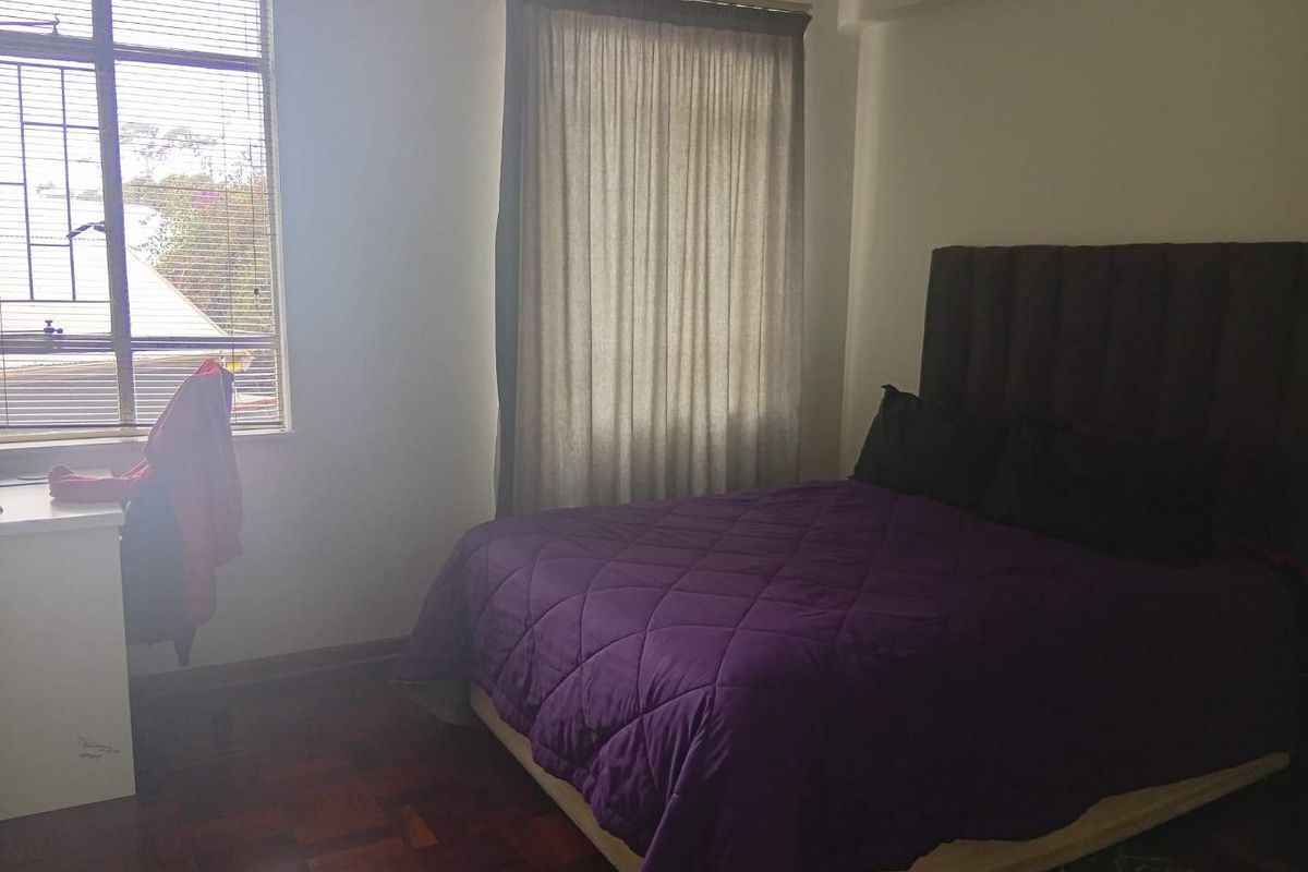 A bedroom featuring parquet flooring and a window with security bars, providing natural light and a functional layout.
