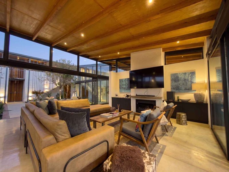 Modern living room featuring a timber-clad ceiling, polished concrete floors, built-in fireplace, and expansive floor-to-ceiling glass walls opening to an outdoor courtyard.