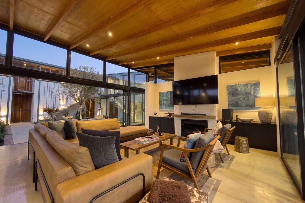 Modern living room featuring a timber-clad ceiling, polished concrete floors, built-in fireplace, and expansive floor-to-ceiling glass walls opening to an outdoor courtyard.