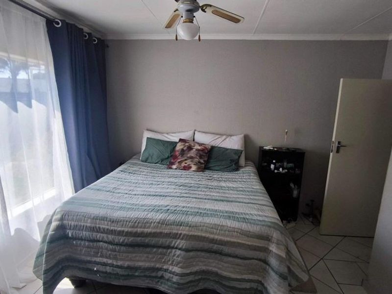 A functional bedroom featuring tiled flooring, a ceiling fan, and natural light from a large window.