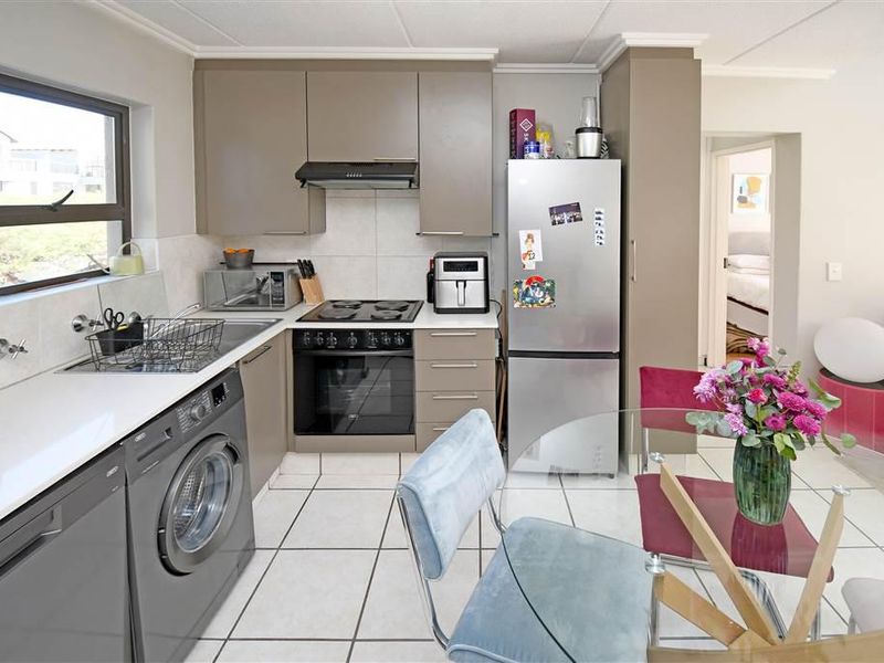 A functional kitchen featuring modern taupe cabinetry, tiled flooring, a built-in oven and hob, and an integrated laundry appliance space.
