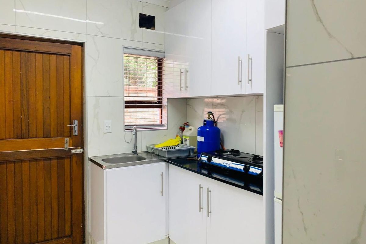Compact kitchen featuring white cabinetry, granite countertops, a gas hob, and tiled finishes, providing a functional prep and cooking space.