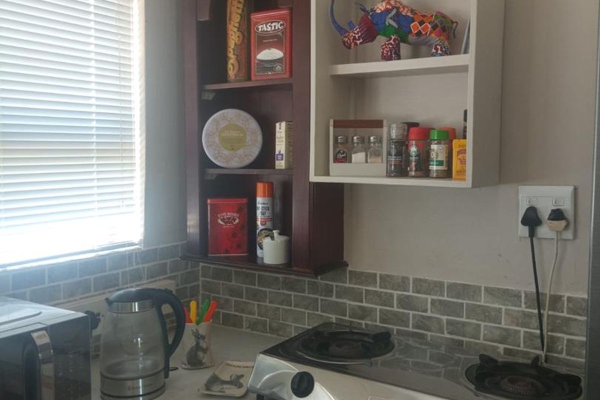 A compact kitchen corner featuring a gas hob, tiled backsplash, and wall-mounted shelving units with a window providing natural light.