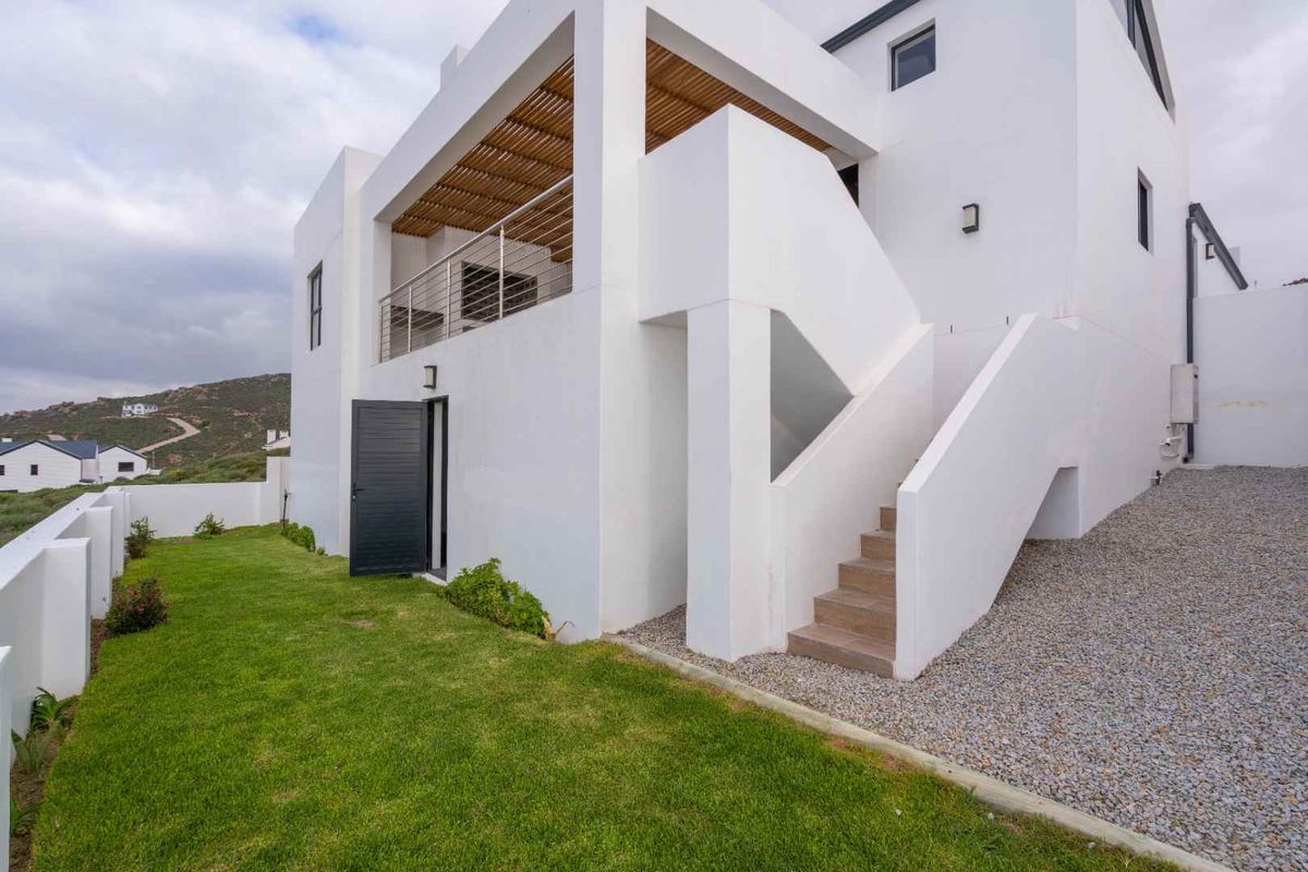 Modern exterior rear view of the house featuring a white facade, covered balcony with timber slats, external staircase, and a landscaped garden area.