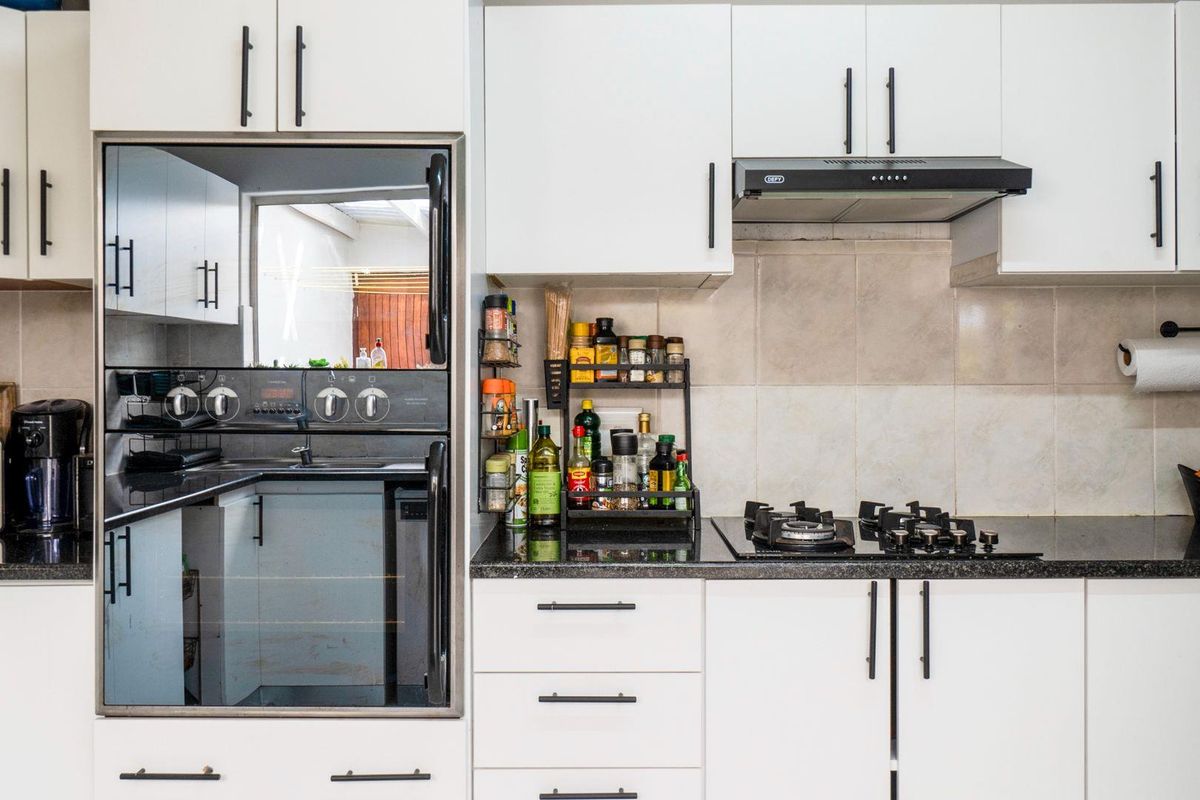 A modern kitchen featuring white cabinetry, black granite countertops, a built-in oven, and a gas hob with an extractor fan.