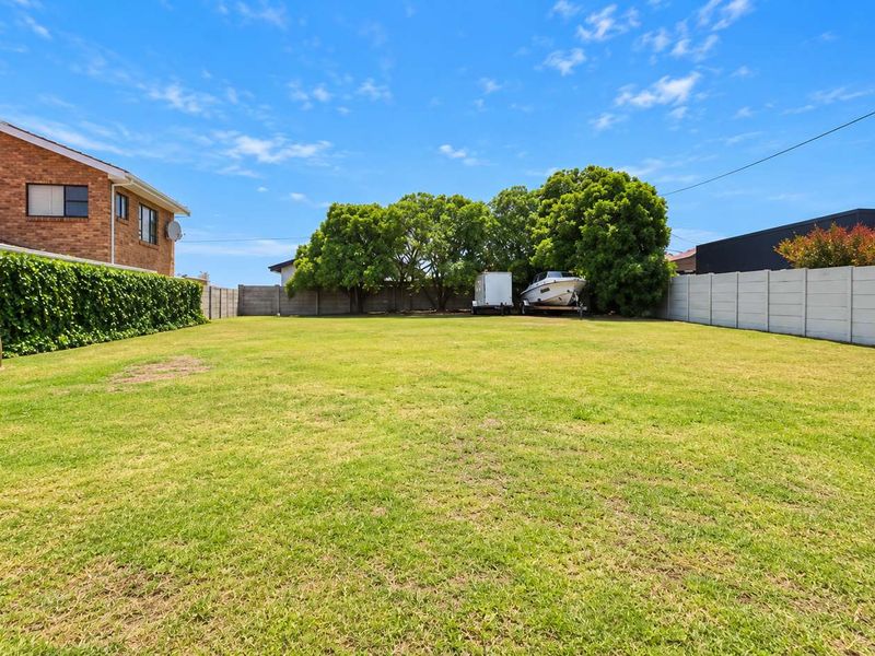 A spacious, well-maintained residential garden featuring a level lawn, mature trees, and secure precast concrete boundary walls.