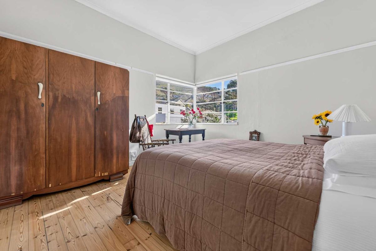 A bright bedroom featuring original timber flooring, a classic picture rail, and corner windows that provide natural light and neighborhood views.
