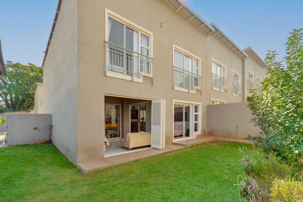 Rear view of a multi-story cluster home featuring a private garden, tiled patio, and upper-level balconies with sliding glass doors.
