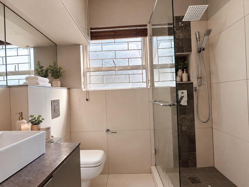Modern bathroom featuring a glass-enclosed shower with rain shower head, wall-mounted toilet, vessel sink, and neutral tiled finishes.