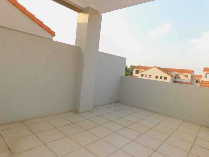 A spacious, covered balcony featuring tiled flooring and solid concrete balustrades, offering an open-air space suitable for outdoor seating.