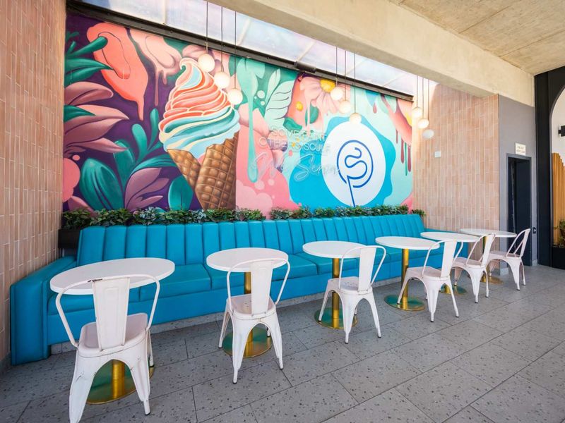 A vibrant, covered outdoor seating area featuring a custom mural, built-in bench seating, and modern pendant lighting on a tiled patio.