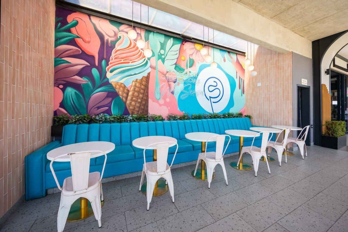 A vibrant, covered outdoor seating area featuring a custom mural, built-in bench seating, and modern pendant lighting on a tiled patio.