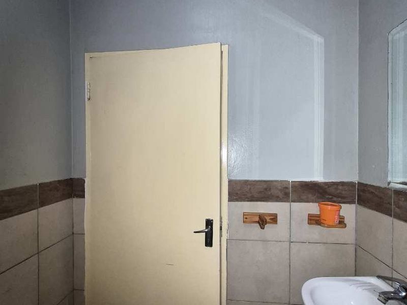A compact bathroom featuring a pedestal washbasin, ceramic wall and floor tiling, and a standard interior door.