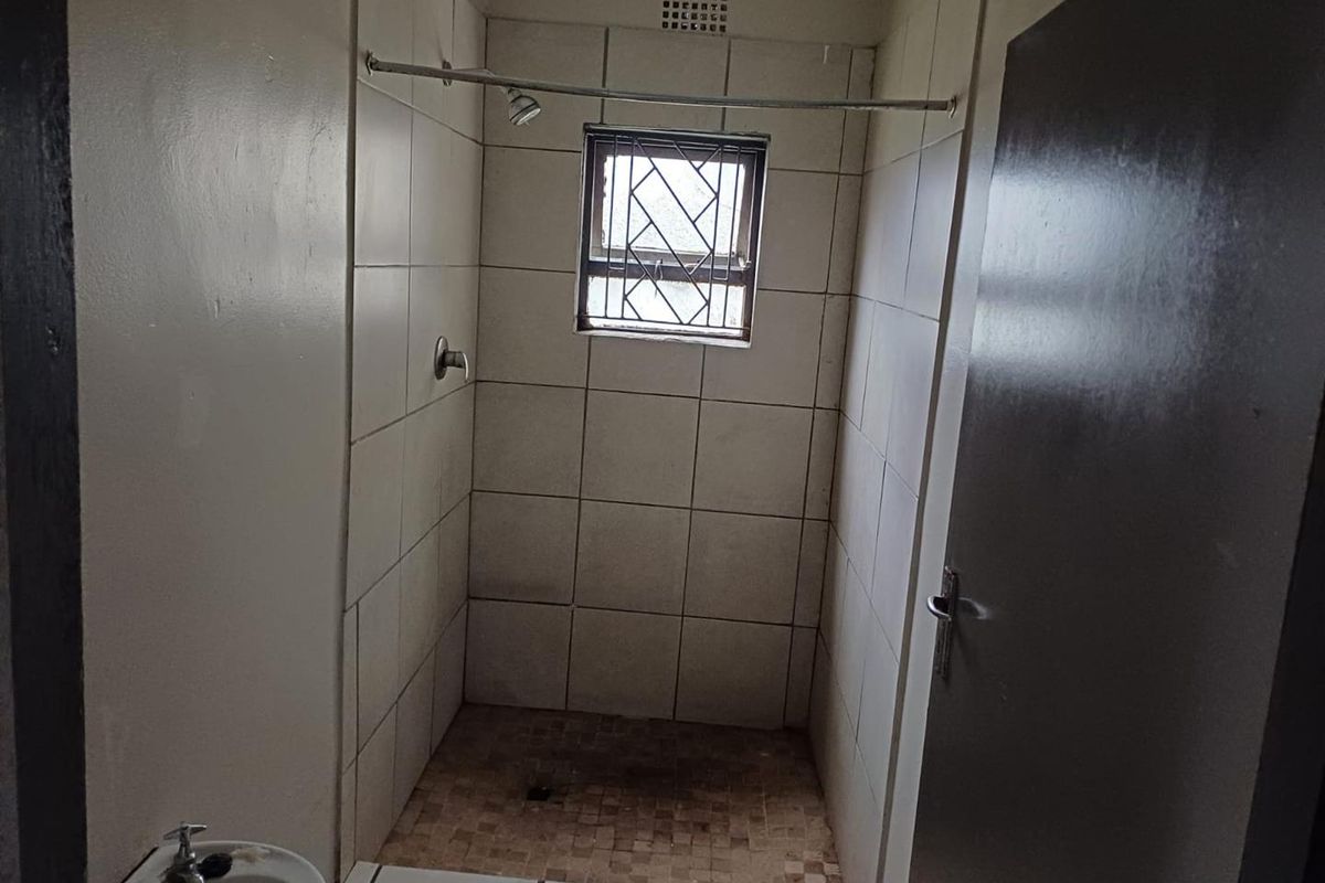 A functional bathroom featuring a tiled shower enclosure with a shower head, a small window with security bars, and a basin.