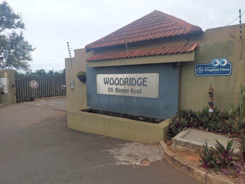 Entrance view of Woodridge complex at 176 Blamey Road, featuring a secure gated access point with electric fencing and established boundary wall.