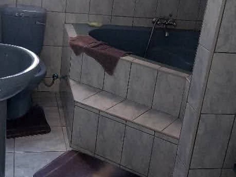 A functional bathroom featuring a corner bathtub, pedestal basin, and toilet, finished with neutral ceramic wall and floor tiling.