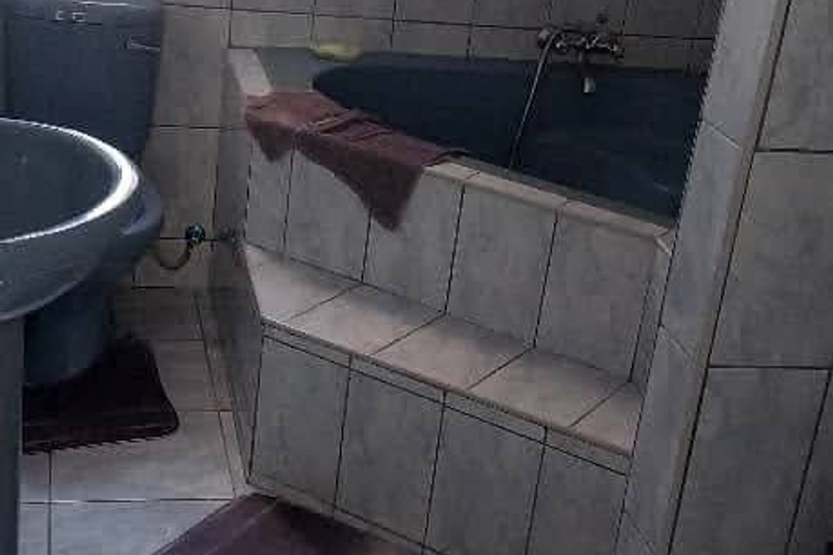 A functional bathroom featuring a corner bathtub, pedestal basin, and toilet, finished with neutral ceramic wall and floor tiling.