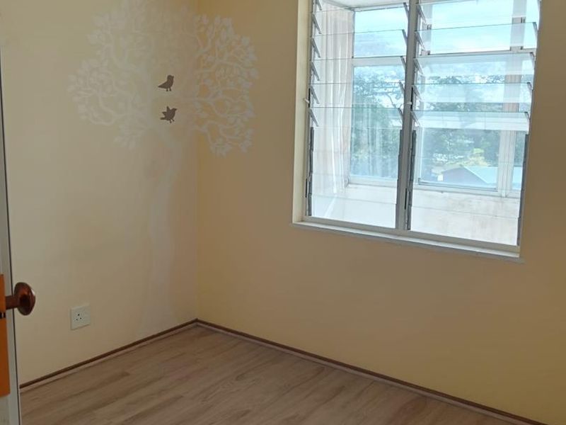 A vacant bedroom featuring light-toned laminate flooring, louver windows, and neutral walls with a decorative decal.