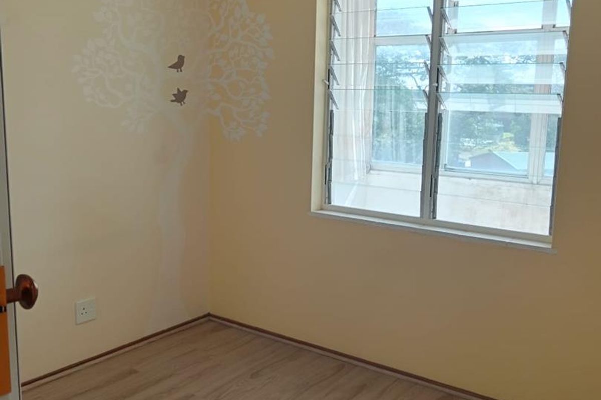 A vacant bedroom featuring light-toned laminate flooring, louver windows, and neutral walls with a decorative decal.