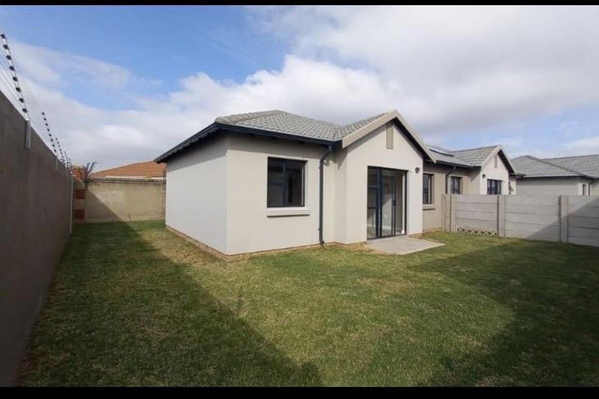Rear view of the townhouse featuring a private garden, paved patio, and secure boundary walls with electric fencing.