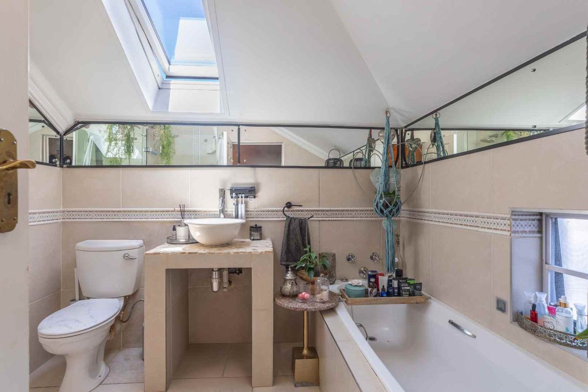A bathroom featuring a built-in vanity with a vessel sink, a bathtub, a toilet, and a skylight providing natural light.