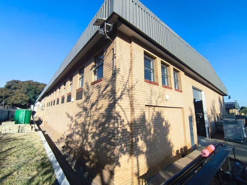 Rear view of an industrial brick building featuring a metal roof, security window bars, and a roller shutter door access point.