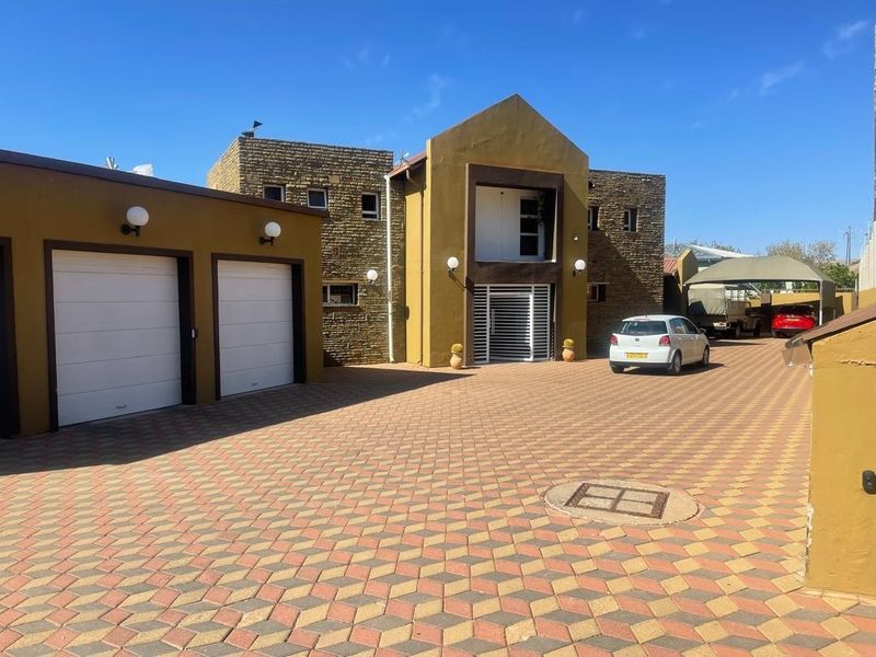 Front elevation of a modern house featuring stone cladding, a double garage, and an extensive paved driveway with additional carport parking.