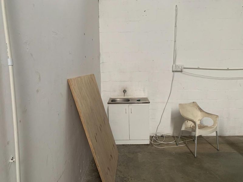 A basic utility space featuring a small sink unit, exposed electrical wiring, and concrete flooring within an industrial setting.