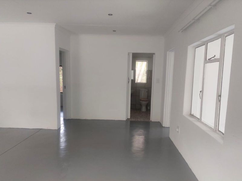An empty, open-plan living area featuring polished grey epoxy flooring, recessed downlights, and white walls, with a view into an adjacent bathroom.