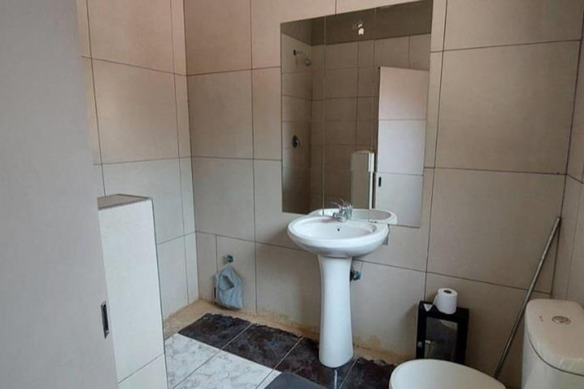 A functional bathroom featuring a pedestal washbasin, wall-mounted mirror, and neutral ceramic wall tiling with contrasting floor tiles.